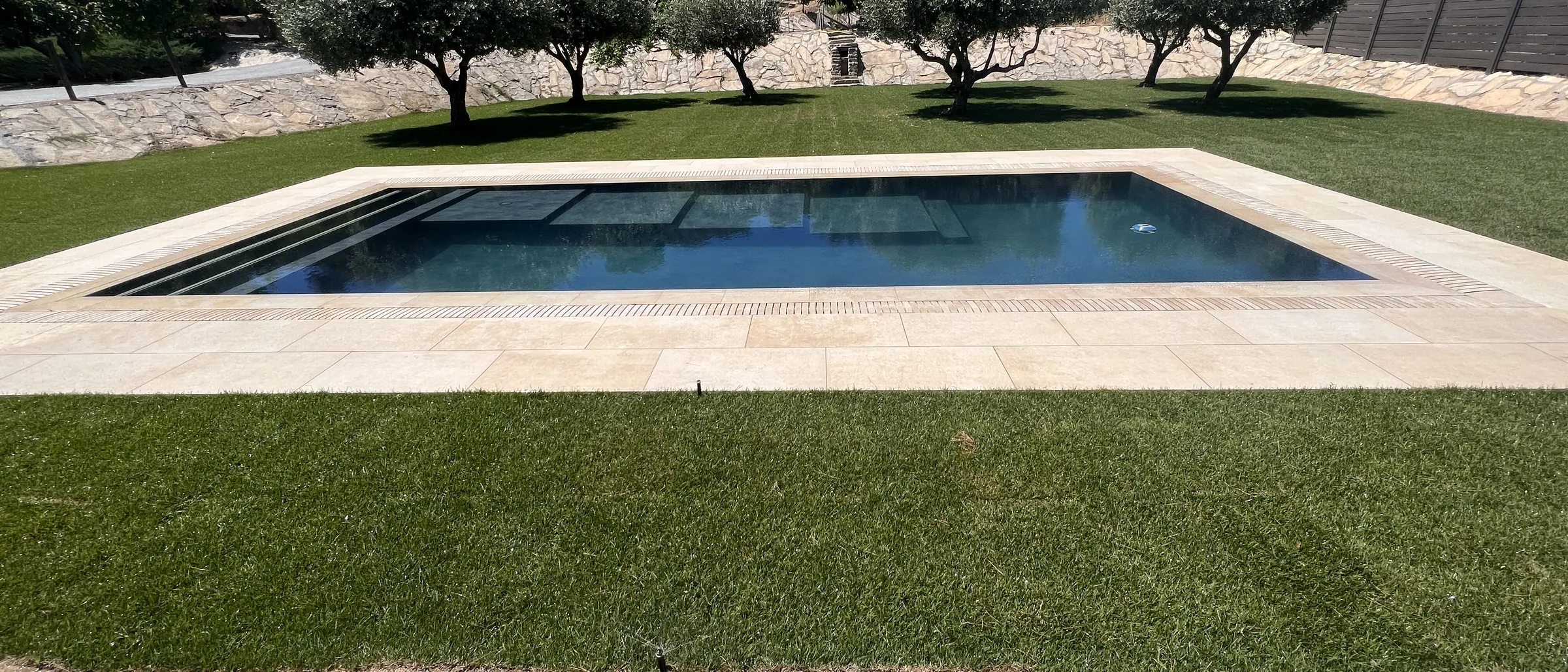 Piscina de obra con coronación de travertino entre olivos, construida por Europiscina